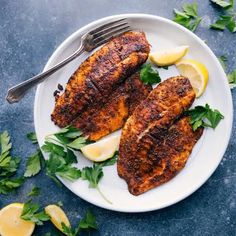 two fish fillets on a plate with lemon wedges and parsley garnish