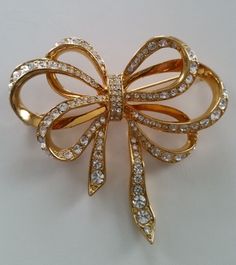 Brilliant KENNETH J LANE Diamanté Crystal Ribbony Bow Brooch Gold Plated Authentic Collectible Designer Vintage Luxury Costume Jewelry... This Beautifully Brilliant Bow brooch hails from Iconic Designer Kenneth J Lane. Signed KJL this Graceful Multi Ribbon Bow design figural is a Stunning example of this Beloved Designer's Extraordinary work. It's a Dazzlingly Feminine piece consisting of row after row of Pavé encrusted Sparkling Diamanté Crystal rhinestones set in a Gleaming Gold plated finish. It's a Classic Beauty with a Wonderful sense of Flowing Movement. Elegant Bows and Pearls take center stage in 2024 bringing this Timeless Beauty to the Forfront of Tastefully Appointed Style. As A Designer Kenneth J Lane captivated the likes of Elizabeth Taylor, Jackie Kennedy Onassis and Princess Ribbon Brooch, Avon Vintage, Bow Brooch, Vintage Ribbon, Antique Brooches, Bow Jewelry, Designer Vintage, Bow Design, Vintage Brooch