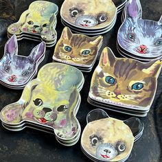 six coasters with cats painted on them sitting on a black surface, one has blue eyes and the other has green eyes