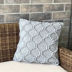 a white pillow sitting on top of a wicker chair next to a brick wall