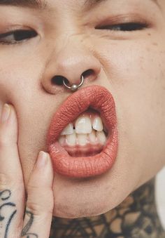 a woman with piercings on her nose is holding her lip up to her mouth