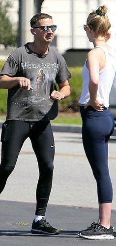 a man standing next to a woman on top of a skateboard in the street