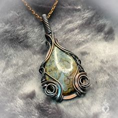 Adorned with a mesmerizing ocean jasper boasting windows of druzy that glisten like sunlight on the water's surface, this pendant exudes an ethereal allure. Its swirly copper design evokes the mysterious charm of the creature from the black lagoon, weaving a tale of enchantment and intrigue. Let this pendant be your talisman of the sea, guiding you through a realm of magic and wonder where the boundaries between reality and fantasy blur, and the secrets of the deep unfold in shimmering splendor. Wire Wrapped Ocean Jasper Pendant Necklaces, Wire Wrapped Ocean Jasper Pendant Necklace, Ocean Jasper Wire Wrapped Pendant Necklaces, Wire Wrapped Ocean Jasper Pendant Jewelry, Artisan Ocean Jasper Jewelry As Gift, Artisan Ocean Jasper Jewelry For Gifts, Ocean Jasper Gemstone Pendant Jewelry, Ocean Jasper Gemstone Pendant, Unique Jasper Pendant Jewelry