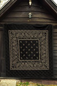 a black and white quilt hanging on the side of a wooden building in front of a light