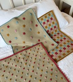 three crocheted pillows on top of a white bed next to two pillow cases