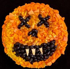 a halloween pizza with black olives, carrots and corn on it's face