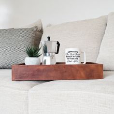 a wooden tray with two coffee cups and a potted plant sitting on top of it