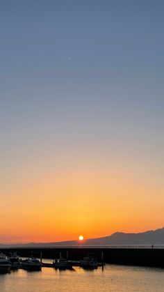 the sun is setting over water with boats in it and mountains in the back ground