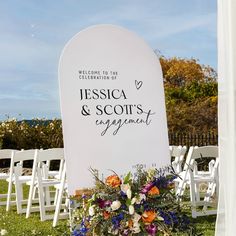 an outdoor ceremony setup with chairs and flowers on the grass, in front of a white backdrop