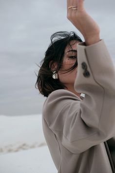 a woman holding her hand up in the air while standing on top of snow covered ground