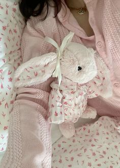 a woman laying in bed with a teddy bear on her stomach and wearing a pink sweater