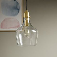 a clear glass light hanging from a ceiling fixture with a gold colored metal fittings