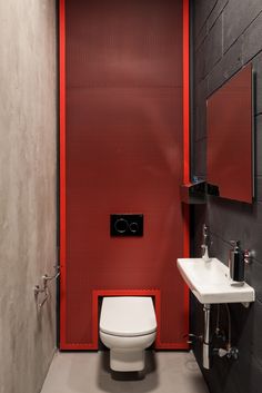 a white toilet sitting in a bathroom next to a sink and red partition on the wall