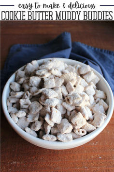 a white bowl filled with cookie butter muddy buddies on top of a wooden table next to a blue towel