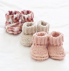 four crocheted baby booties are lined up on a white surface, one is pink and the other is beige