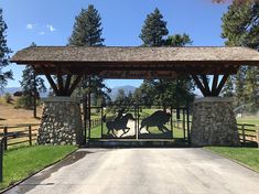 a gated entrance to a horse ranch with two horses running through it and trees in the background