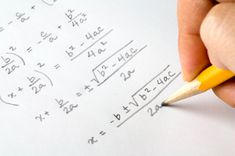 a person is holding a pencil and writing on paper with graphing numbers in the background