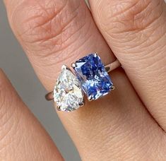 a woman's engagement ring with two pear shaped blue and white diamonds on it