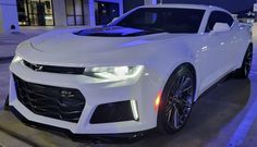 a white chevrolet camaro parked in front of a building