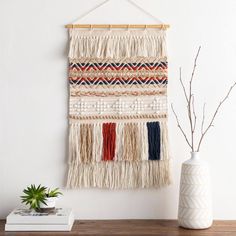 the wall hanging is decorated with different colored fringes and beads, along with a plant in a white vase