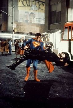 a man in a superman costume is being pushed by another man on the street with other people around him