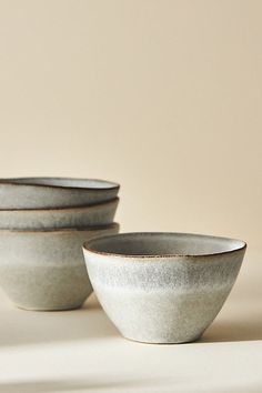 three white bowls sitting next to each other on top of a table with a beige wall in the background