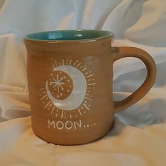 a ceramic mug with the moon and stars on it is sitting on a white sheet