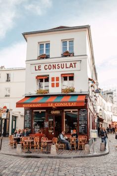 people sitting at tables in front of a restaurant on a cobblestone street corner