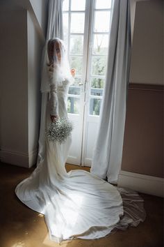 a woman in a wedding dress standing next to a window