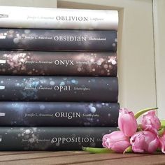 a stack of books sitting on top of a wooden table next to pink tulips