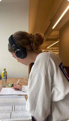 a woman sitting at a desk with headphones on and writing in a notebook while wearing headphones