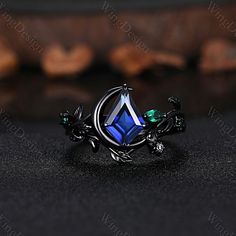 a ring with blue and green stones on it sitting on a black surface next to some nuts