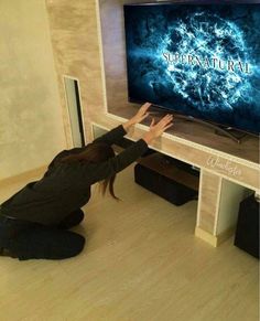 a woman kneeling on the floor in front of a large screen tv that reads supernatural