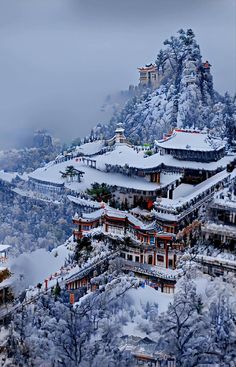 an aerial view of a snow covered mountain with buildings and trees in the foreground