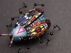 a colorful bug sitting on top of a gray floor next to black balls and screwdrivers