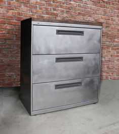 a metal filing cabinet sitting in front of a brick wall with two drawers on each side