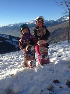 two young children standing in the snow with their snowboards on top of a mountain