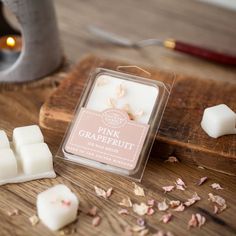 pink grapefruit wax cubes on a wooden cutting board next to a candle