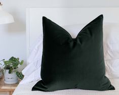 a black pillow sitting on top of a bed next to a night stand and lamp