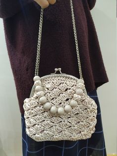 a woman is holding a white purse with pearls on the front and chain around it