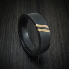 a black and gold wedding ring with two stripes on the inside, sitting on a wooden surface