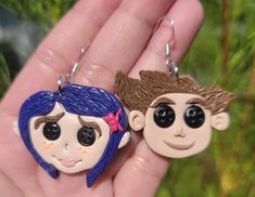 there are two key chains in the palm of someone's hand, one is wearing a hat and the other has a doll face on it