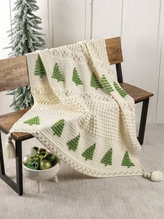 a crocheted blanket sitting on top of a wooden bench next to a tree