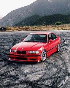 a red car parked on top of a parking lot with mountains in the back ground