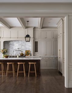 a large kitchen with white cabinets and wood flooring is pictured in this image, there are stools at the center of the island