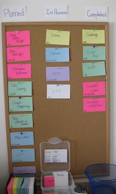 a bulletin board with sticky notes attached to it and plastic bins on the desk