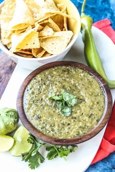 a bowl of guacamole next to a plate with chips and limes