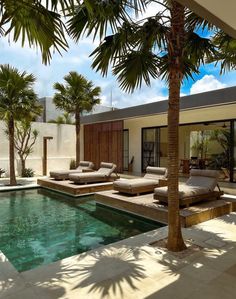 an outdoor swimming pool with lounge chairs and palm trees in the foreground, next to a house