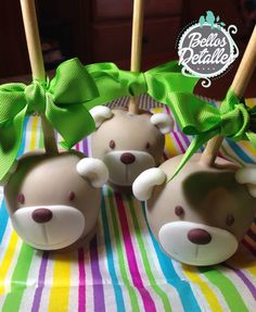 three cake pops decorated like bears with green bows on them sitting on a striped tablecloth