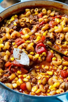 a large pot filled with pasta and meat on top of a blue table cloth next to utensils